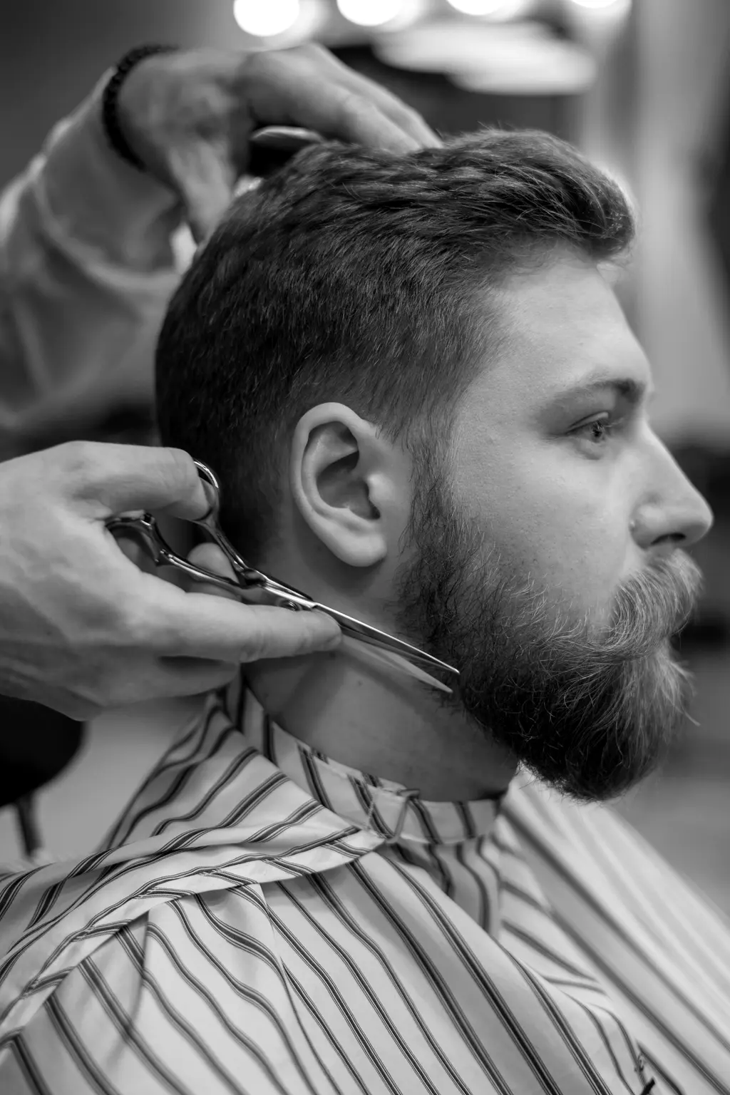 Barbero perfilando la barba de un cliente con camisa de rayas