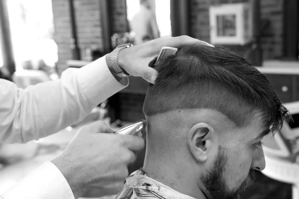 Barbero repasando con los dedos el corte de un cliente con barba