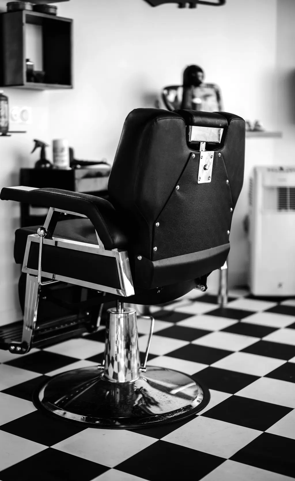 Sillón de barbero de cuero negro sobre suelo de baldosas en damero